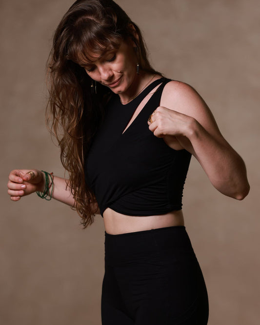 Woman in black athletic wear from Alchemy Yoga line posing against a brown background