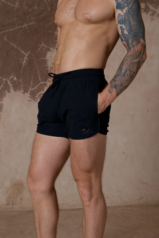 Man wearing black swim shorts against a textured brown wall