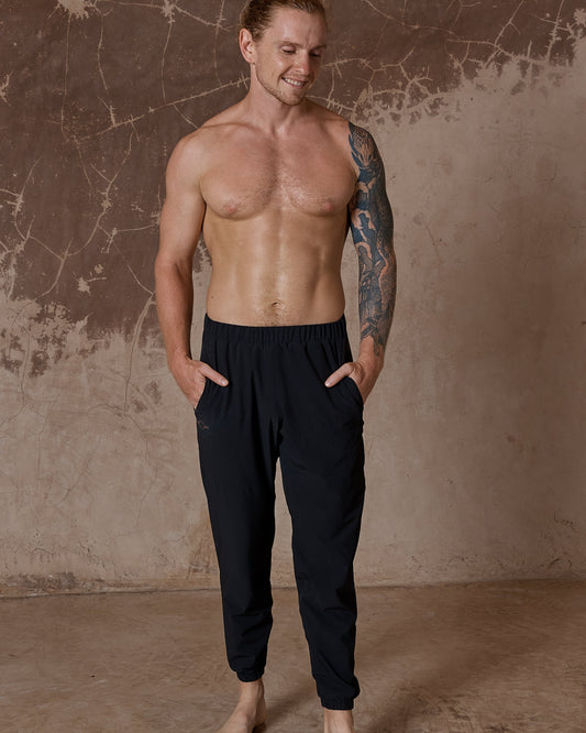 Man wearing black pants standing against a textured brown wall.